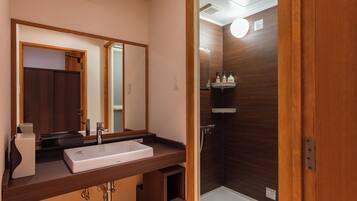 A bathroom with a wooden vanity, a sink, a mirror, and a shower area.