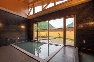 Piscina com barreira de vidro, vigas de madeira no teto e vista para uma montanha.