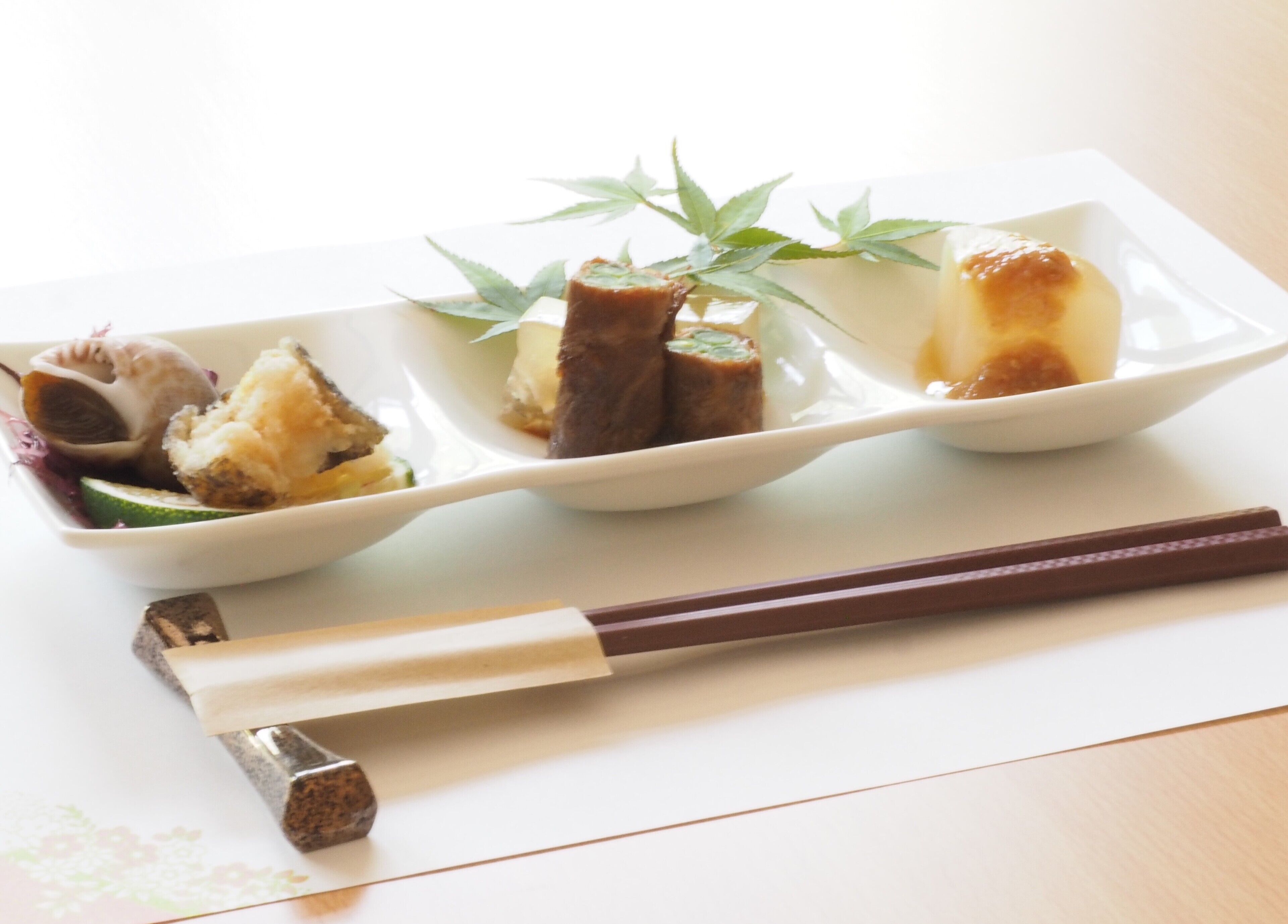 A white rectangular plate with various food items and chopsticks on a table.