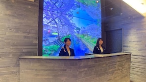 A reception desk with a digital display of a scenic landscape, a stone wall, and a wooden reception counter. - J Hotel Tokyo Geo (Tokyo)