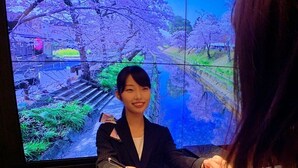 A person seated at a table with papers, in front of a large screen displaying a scenic view. - J Hotel Tokyo Geo (Tokyo)