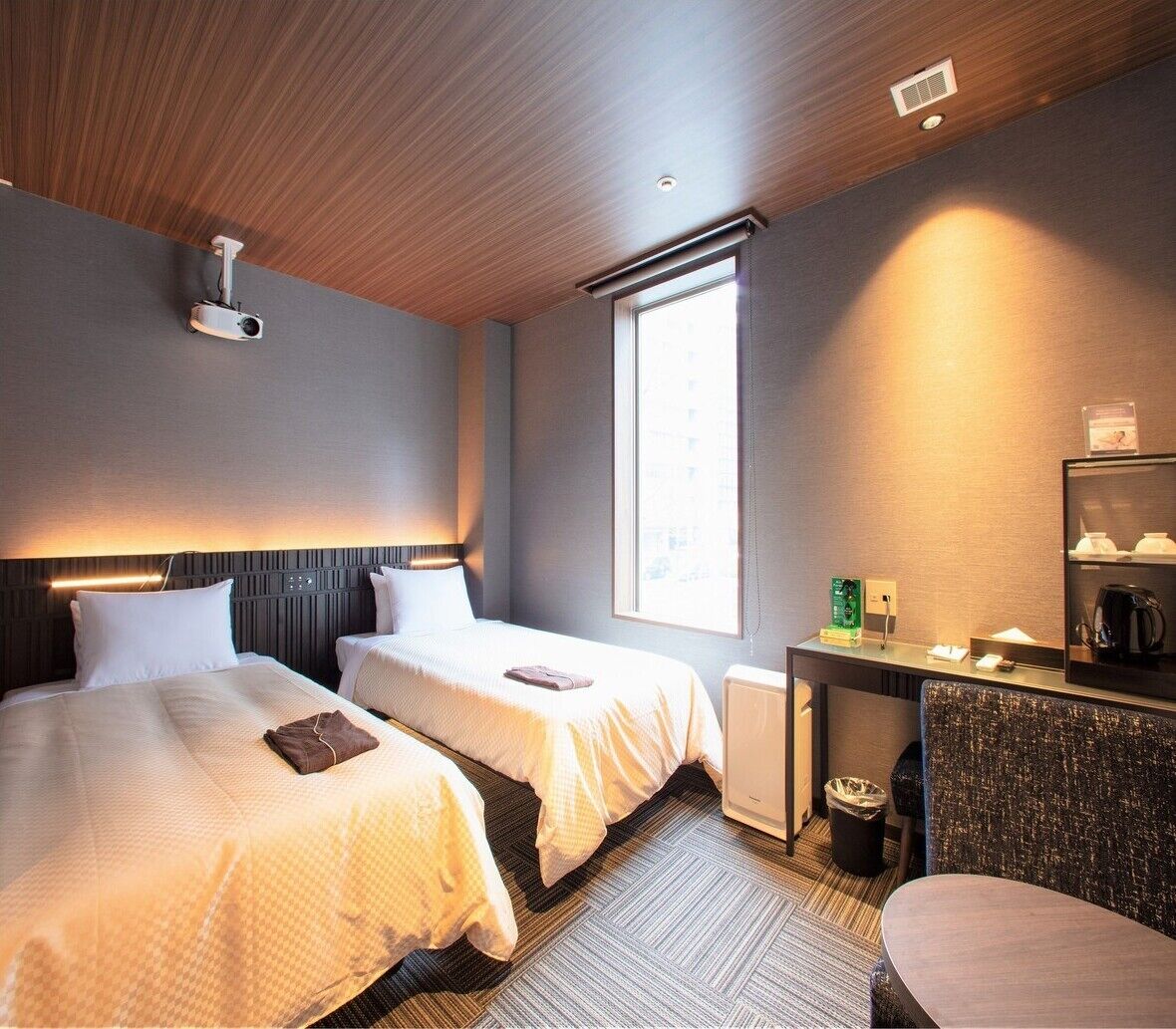 A hotel room with two beds, a desk with a mirror, a coffee machine, and a window.