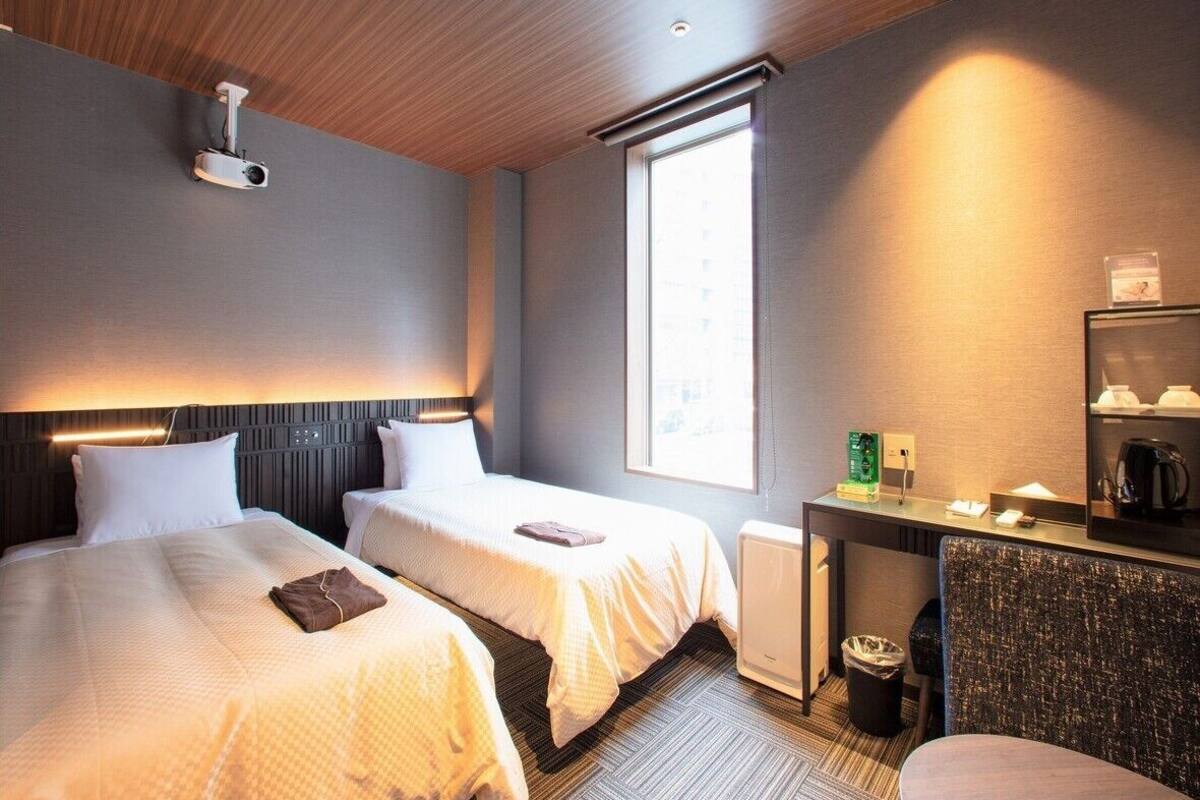 A hotel room with two beds, a desk with a mirror, a coffee machine, and a window.