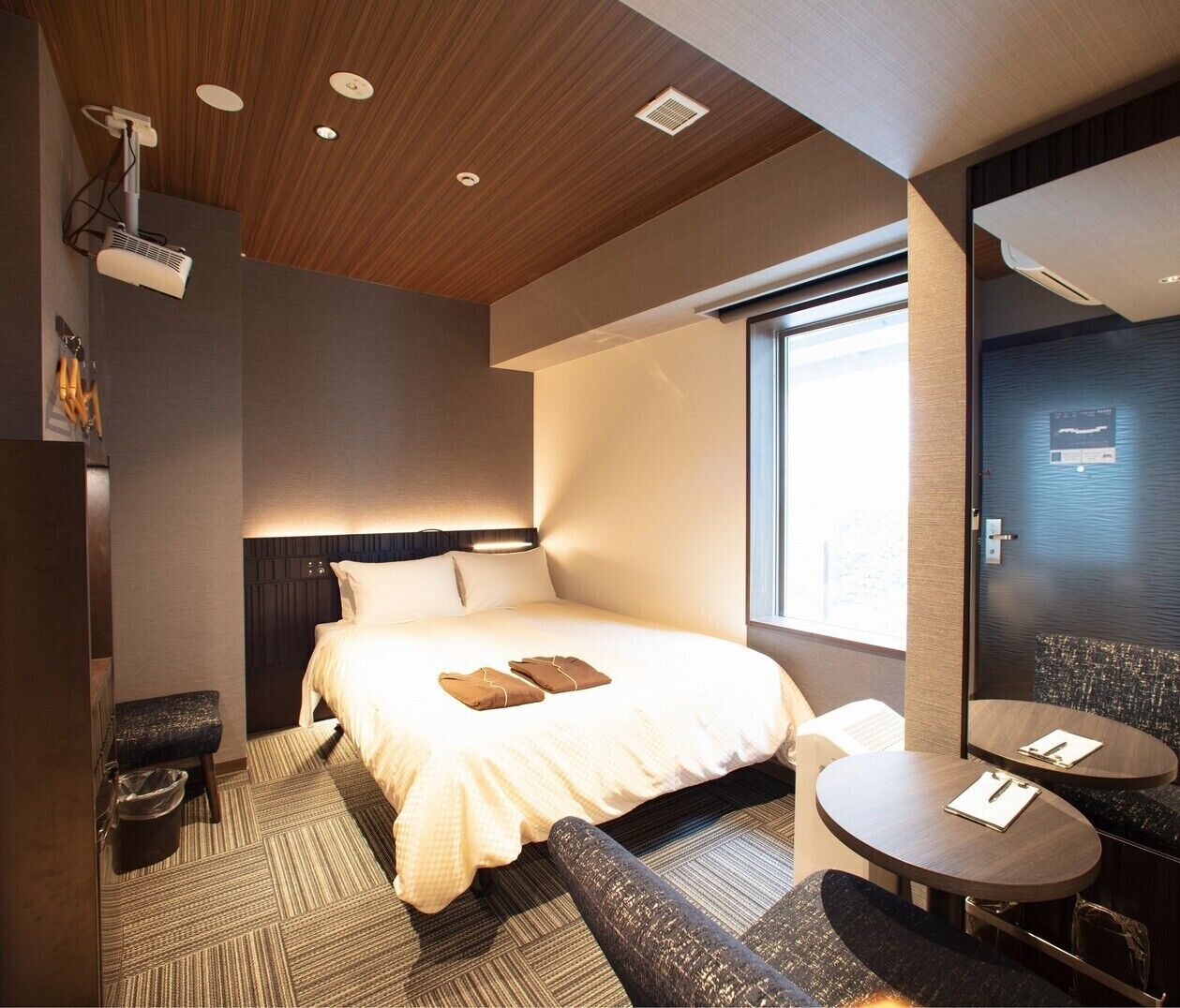 A hotel room with a bed, bedside table, chair, and a large window.