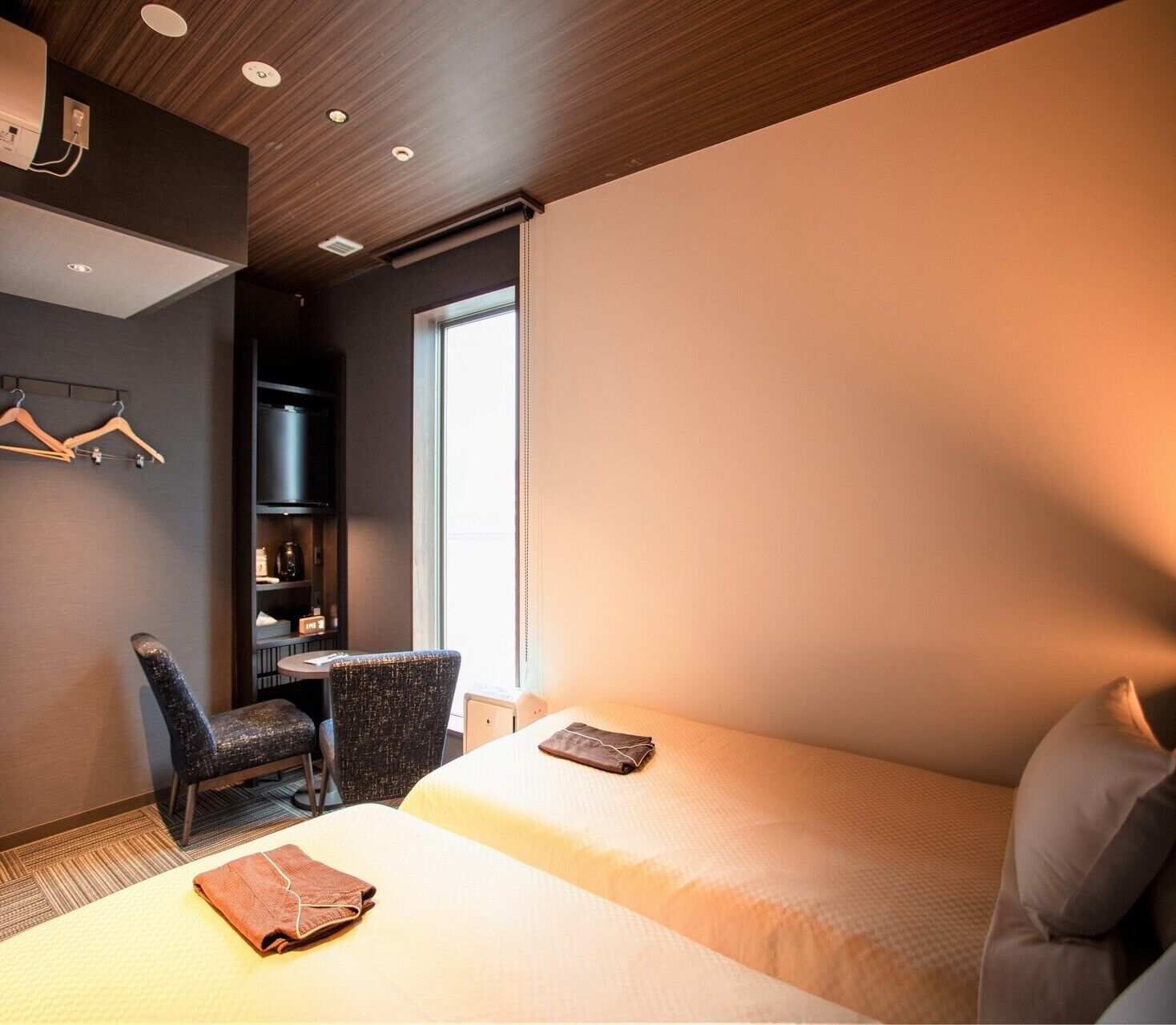 A hotel room with two beds, a desk, a chair, and a wardrobe.