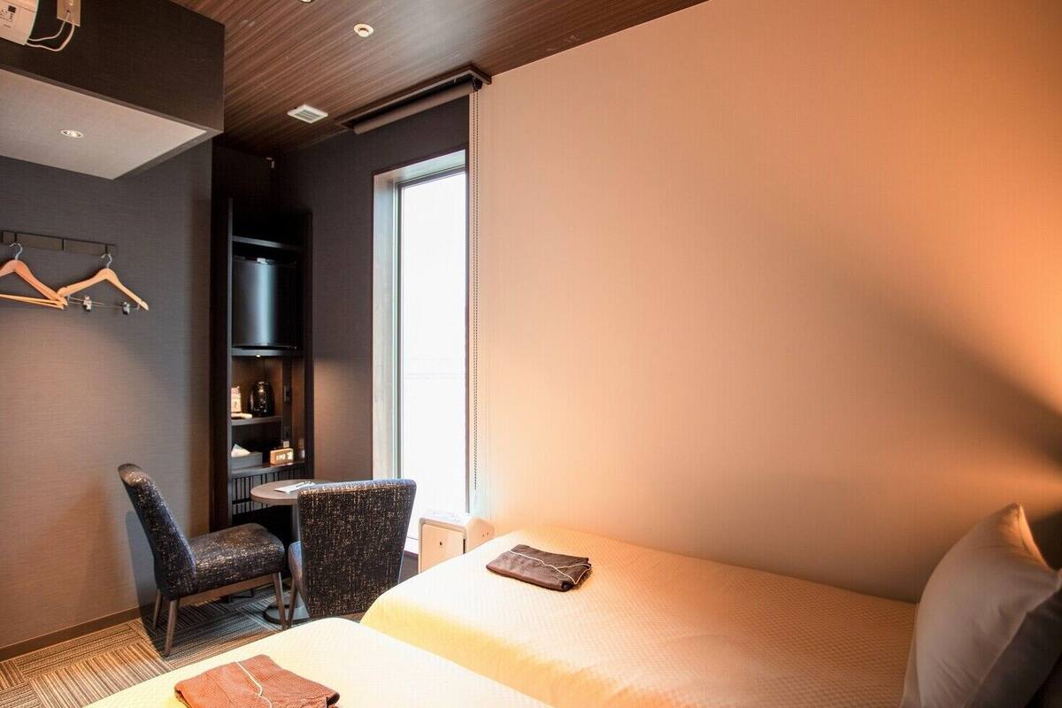 A hotel room with two beds, a desk, a chair, and a wardrobe.
