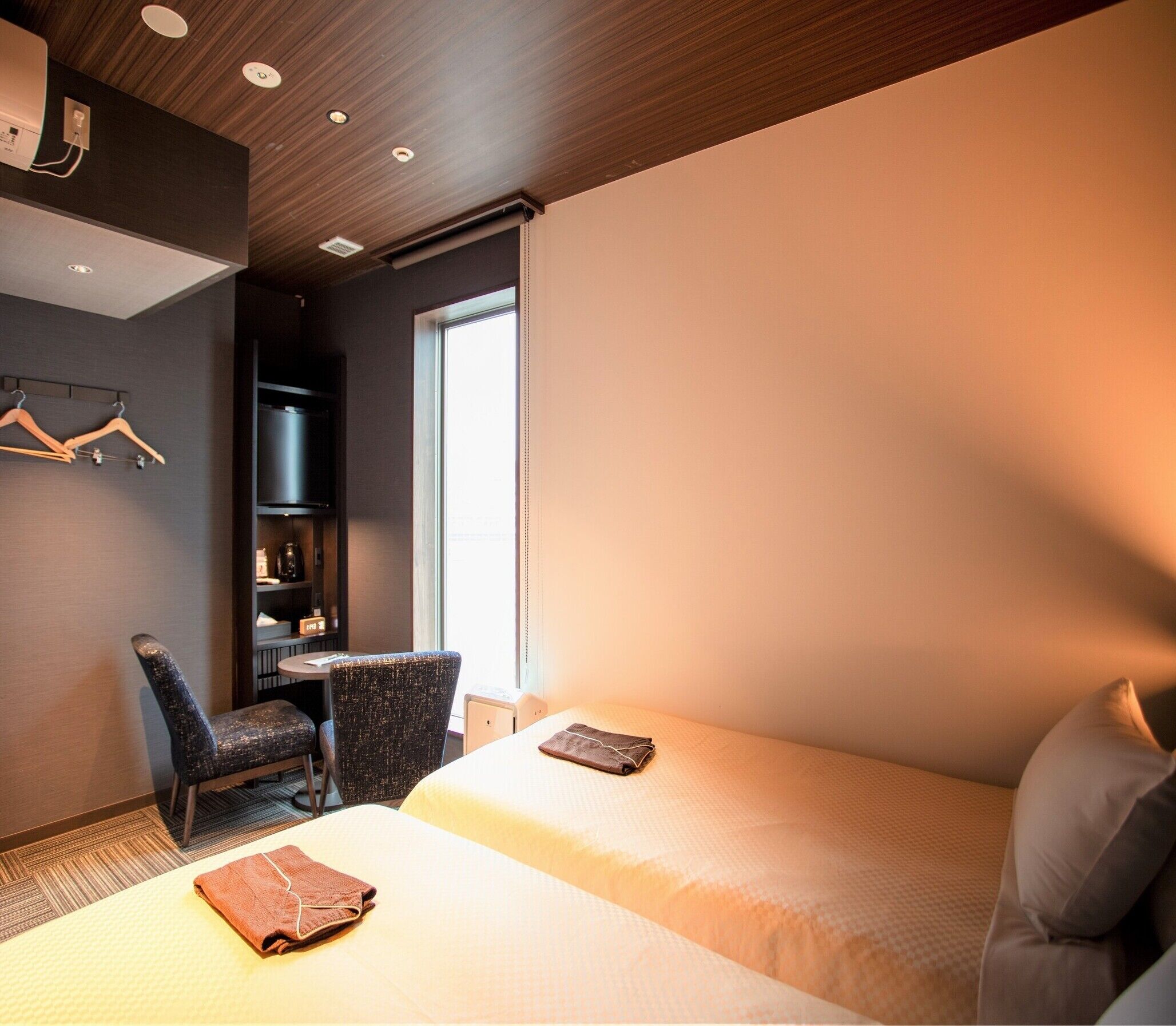A hotel room with two beds, a desk, a chair, and a wardrobe.