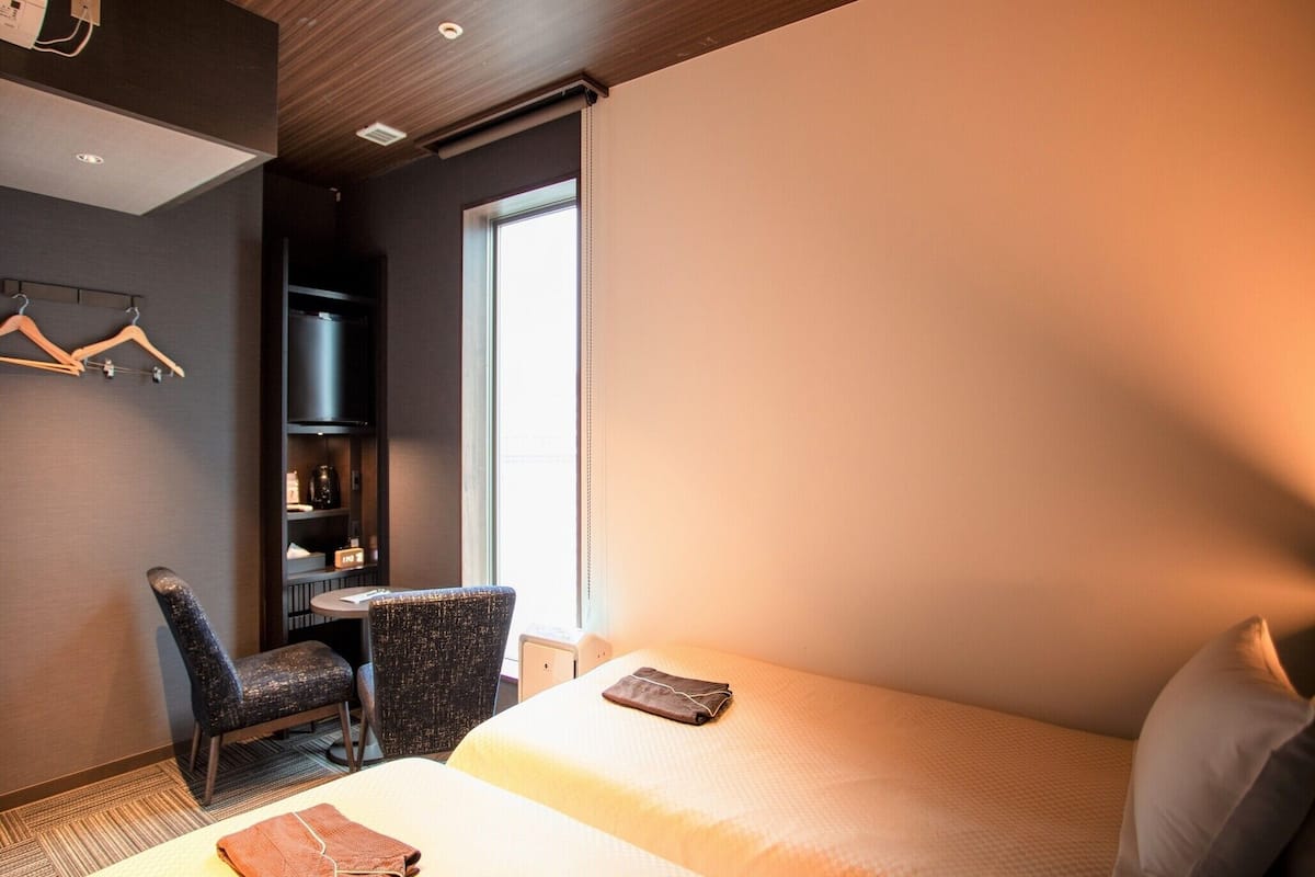 A hotel room with two beds, a desk, a chair, and a wardrobe.