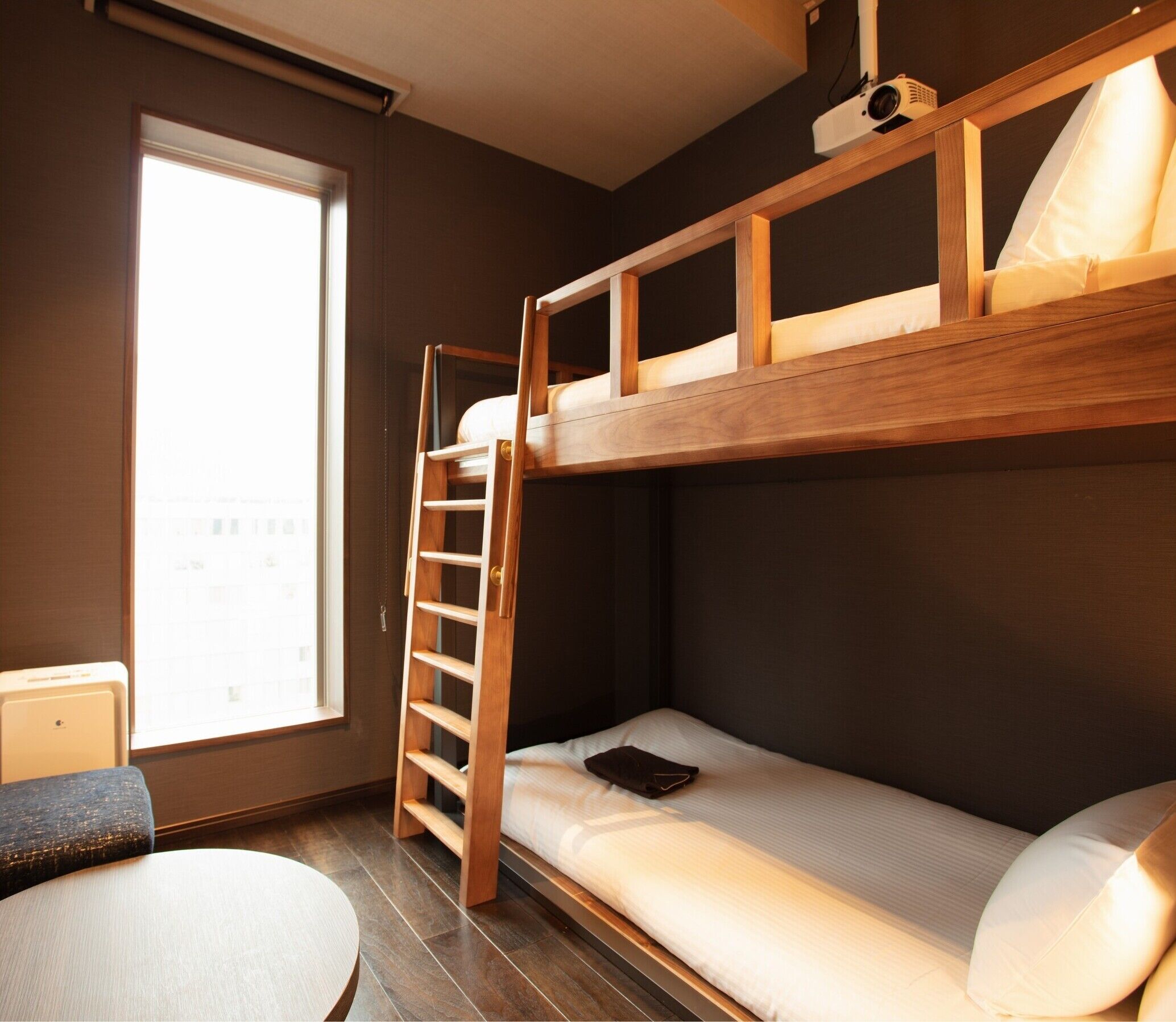 A bunk bed with a wooden ladder, a small table, and a window with a view.