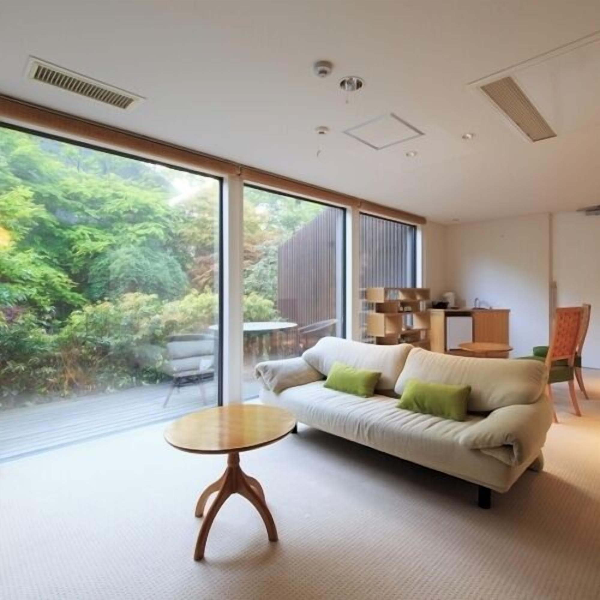 Una sala de estar moderna con un sofá, una mesita redonda y vistas al exterior con vegetación.