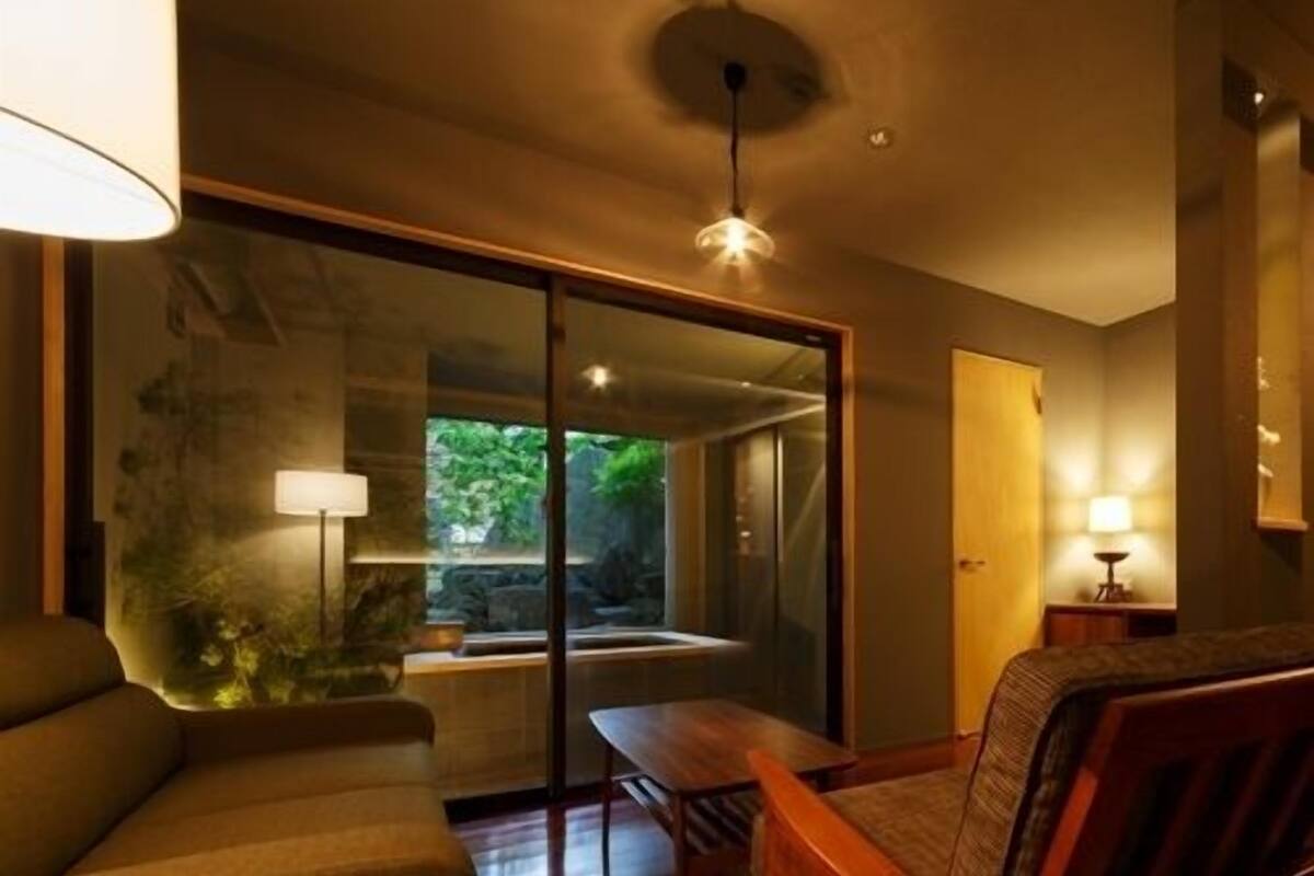A modern interior with a sofa, a wooden table, and a glass door leading to a garden.