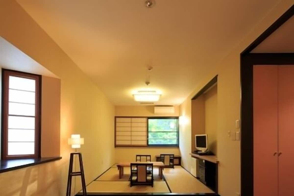 A hotel room with two beds, a television, a desk with a chair, a window, and a sliding door.