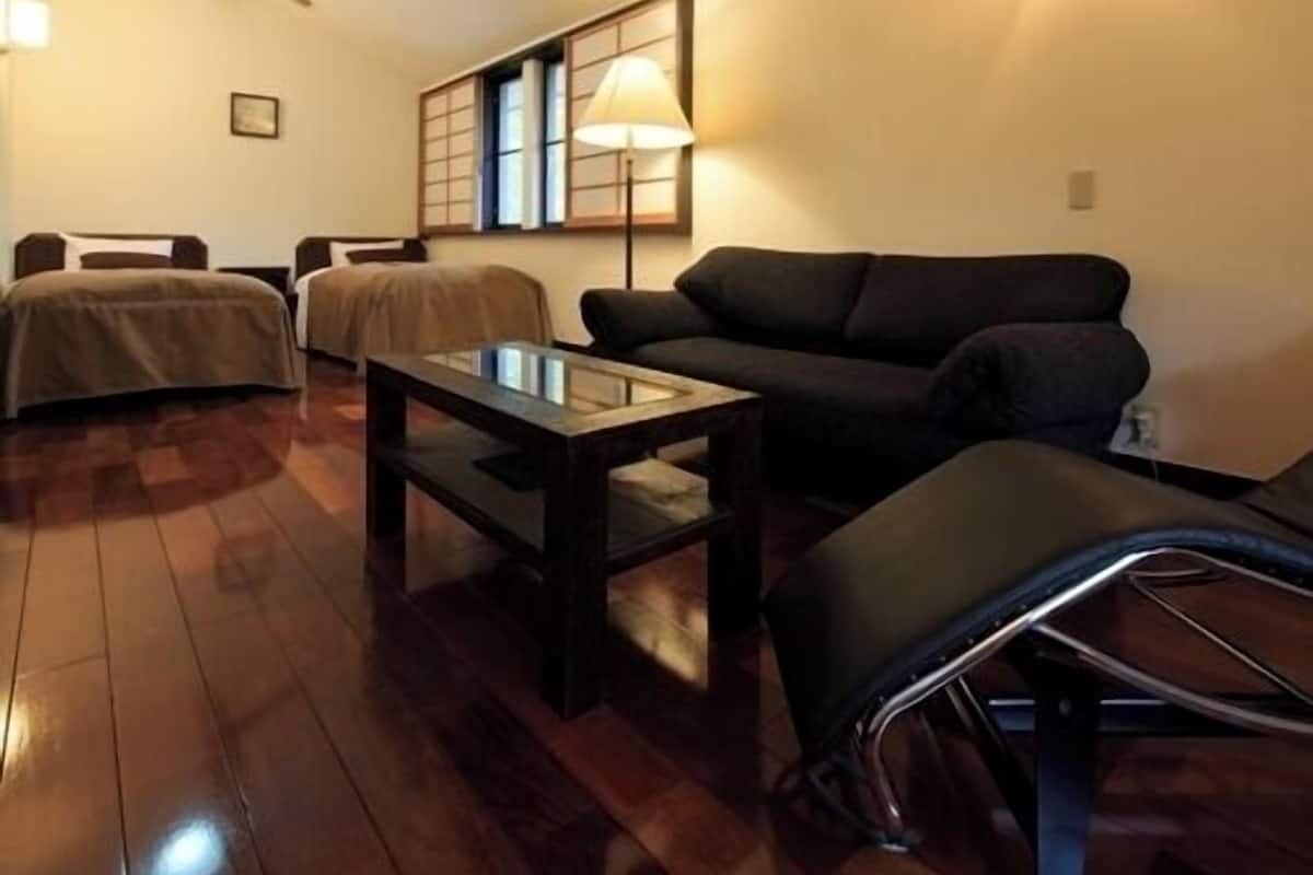 A room with a bed, a sofa, a table, and a lamp.