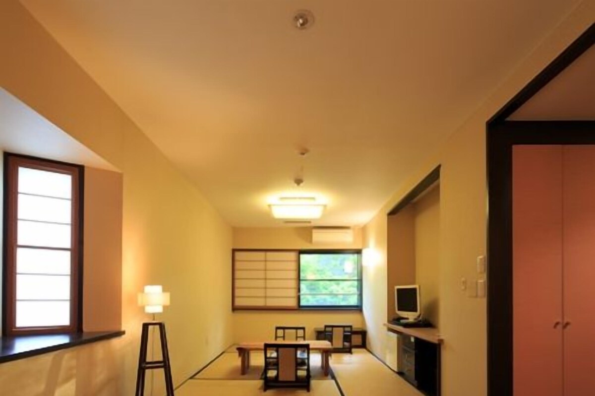 A hotel room with two beds, a television, a desk with a chair, a window, and a sliding door.