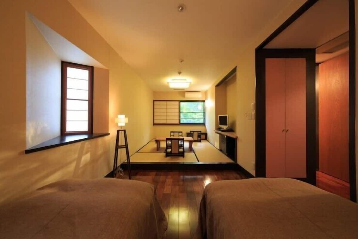 A traditional Japanese-style room with tatami flooring, a low table with cushions, a television, and sliding doors.