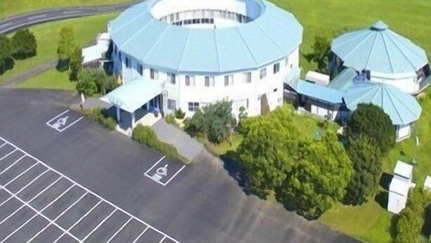 Un bâtiment circulaire doté d’une cour intérieure, entouré d’un parking et d’espaces verts.