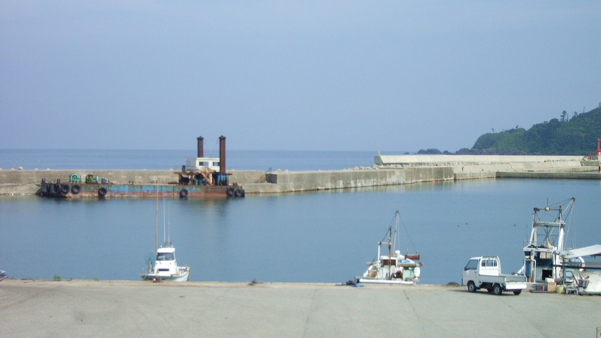 A marina with boats docked, a crane, and a building with two smokestacks.