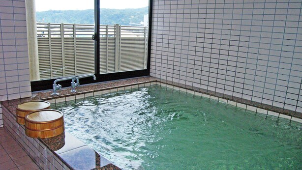 A small indoor hot tub with a view of a bridge and hills. - Rokko Ryokan (Suzu)