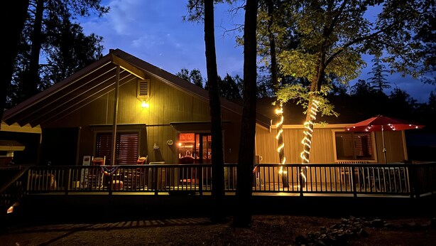 A wooden cabin with a porch, a small attached structure, and a fence.