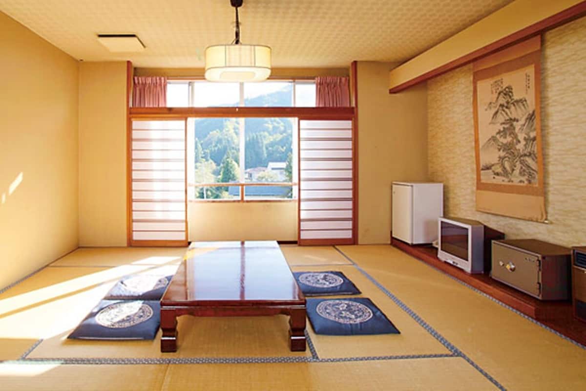 Una habitación japonesa tradicional con suelo de tatami, una mesa baja, puertas correderas shoji, un televisor y un refrigerador.