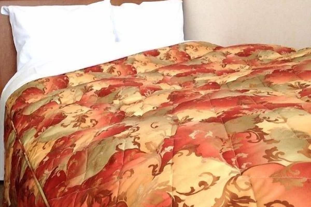 A bed with a floral patterned bedspread, white pillows, and a wooden headboard.