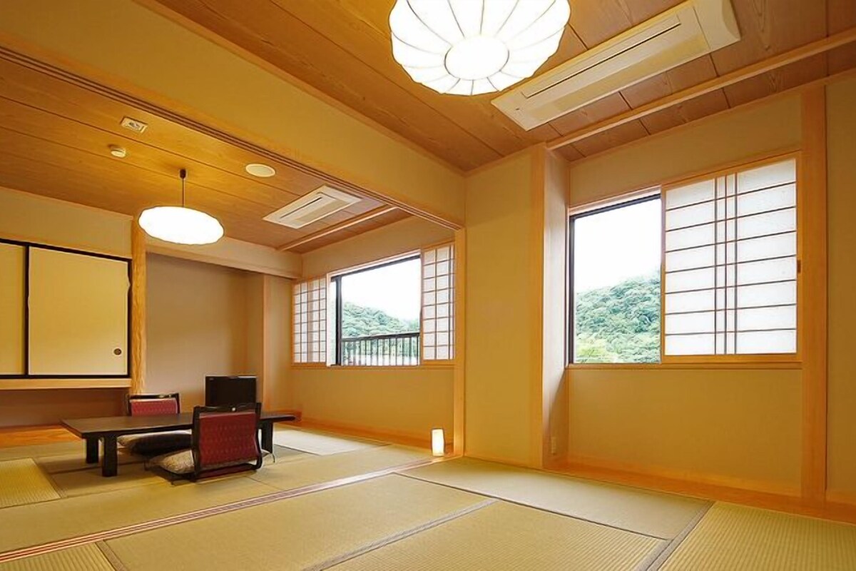 A traditional Japanese room with tatami flooring, a low table with a cushion, a television, and sliding doors.