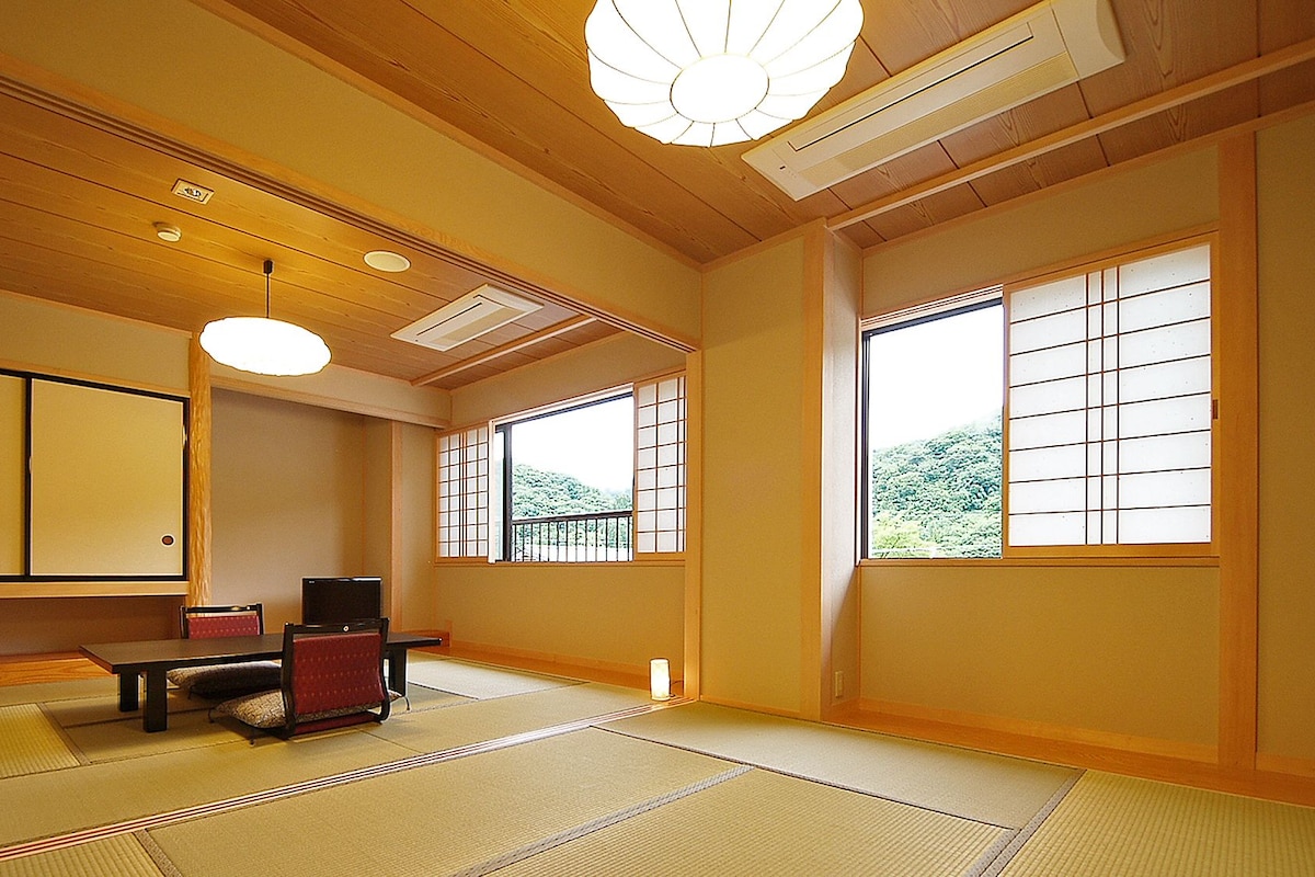 A traditional Japanese room with tatami flooring, a low table with cushions, a television, and sliding doors.