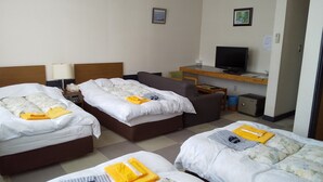 Habitación de hotel con tres camas, televisión, escritorio pequeño y una caja fuerte.