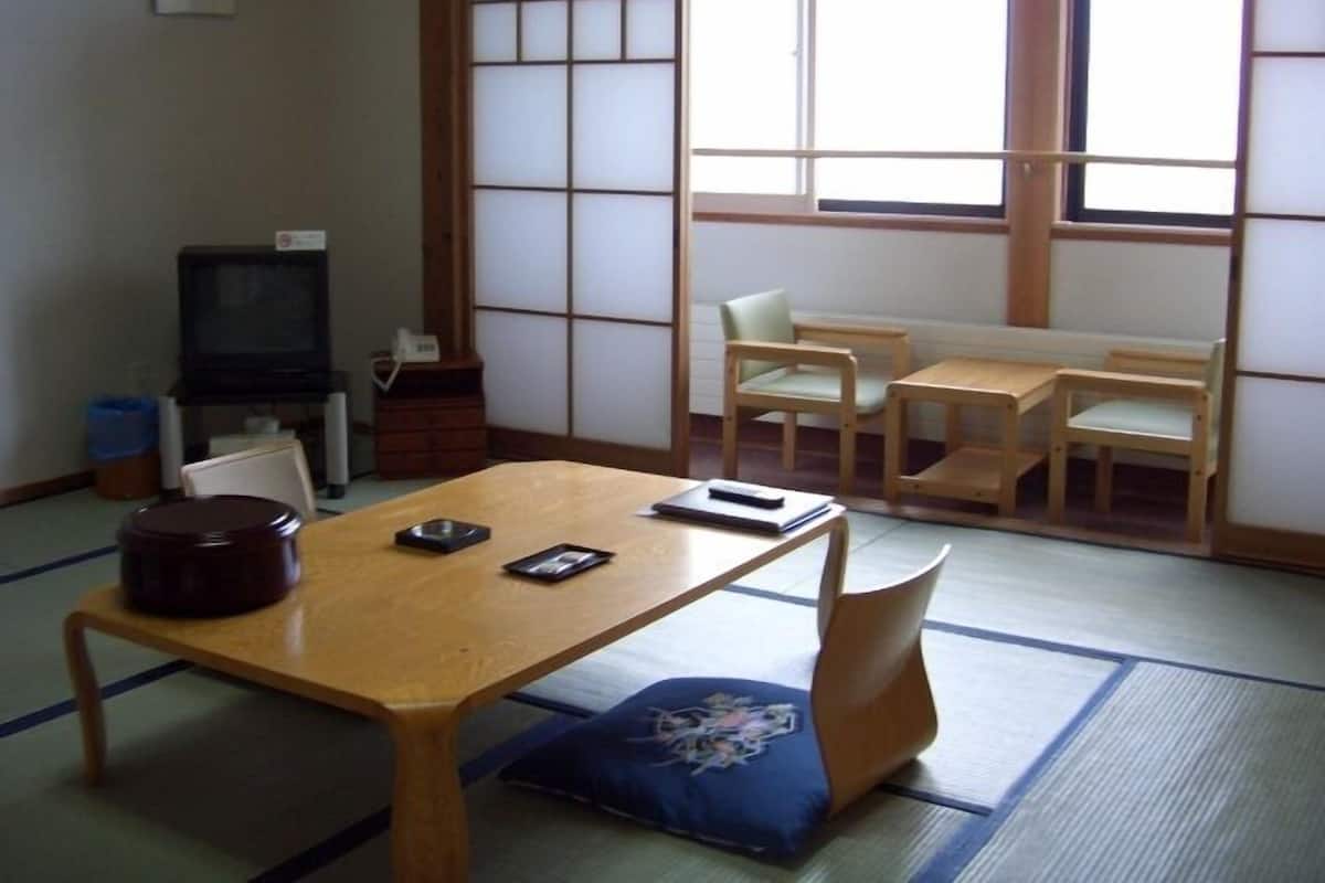 A traditional Japanese room with tatami flooring, a low table, wooden chairs, and a television.