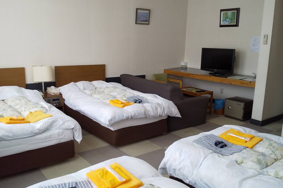 A hotel room with three beds, a TV, a small desk, and a safe.