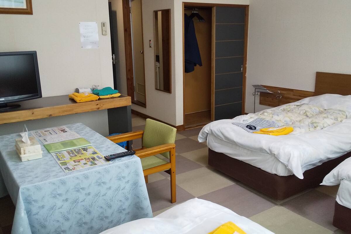 A hotel room with a bed, a desk with a computer, a chair, a TV, and a wardrobe.