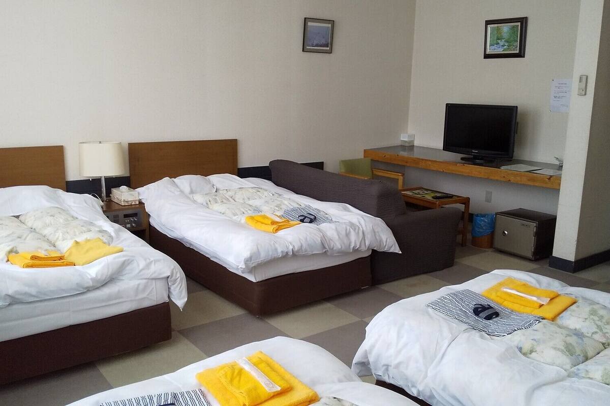 A hotel room with three beds, a television, a desk, and a chair.