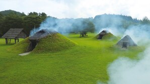 Casas tradicionales cubiertas de césped con humo elevándose, en un paisaje verde.