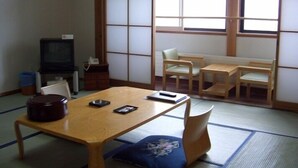 Una habitación japonesa tradicional con suelo de tatami, una mesa baja, sillas, televisor y puerta corredera.