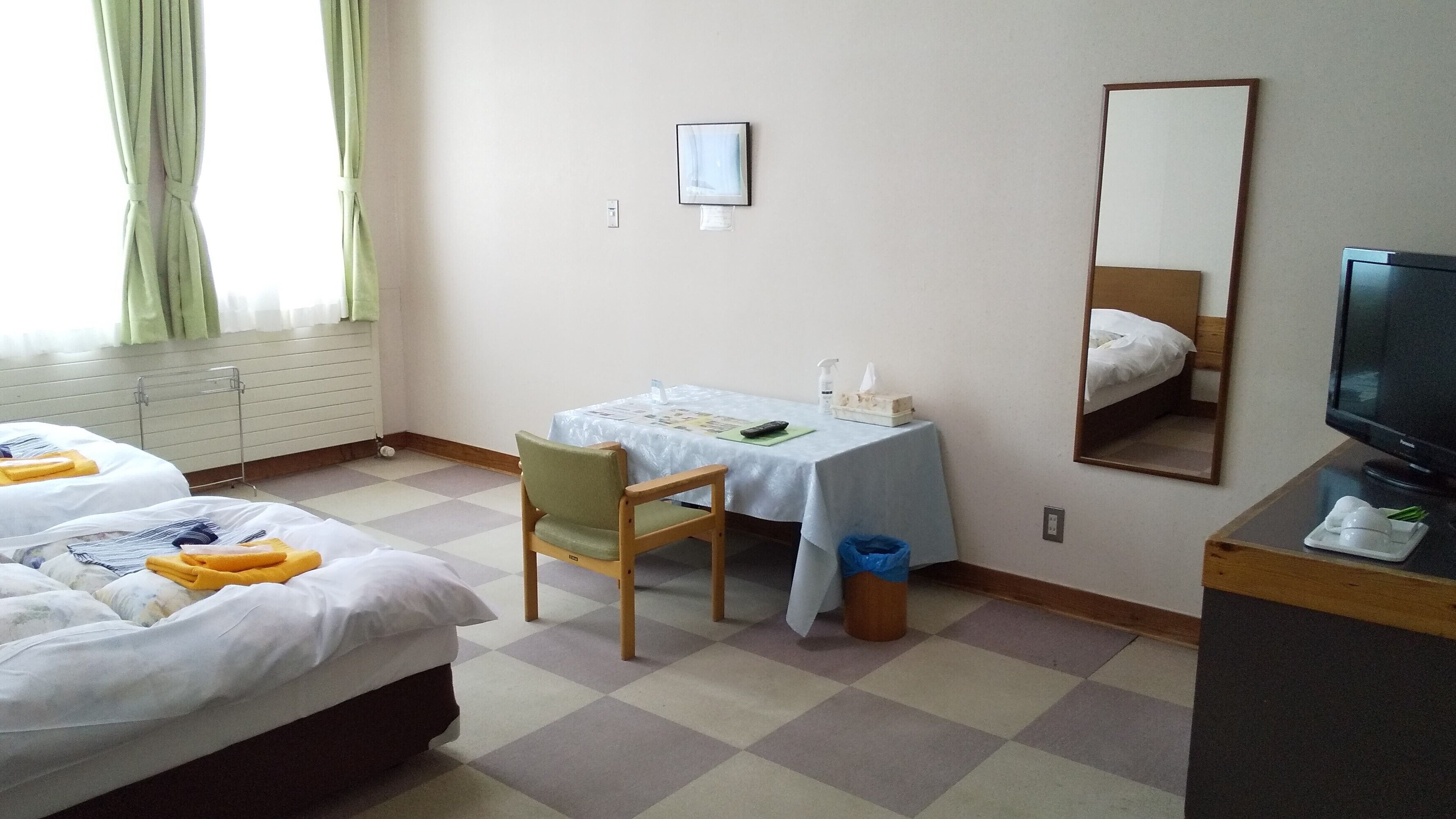 Una habitación de hotel con dos camas, un escritorio con silla, un televisor y un espejo.