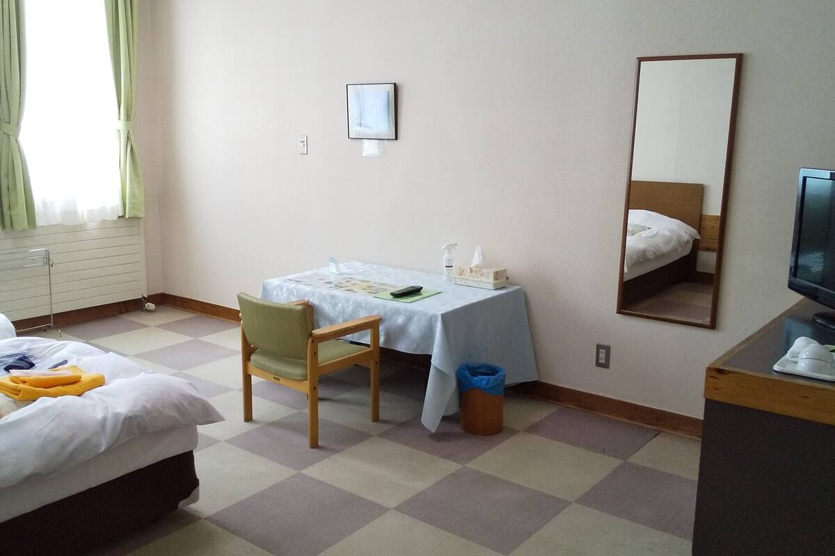 A hotel room with two beds, a desk with a chair, a television, and a mirror.