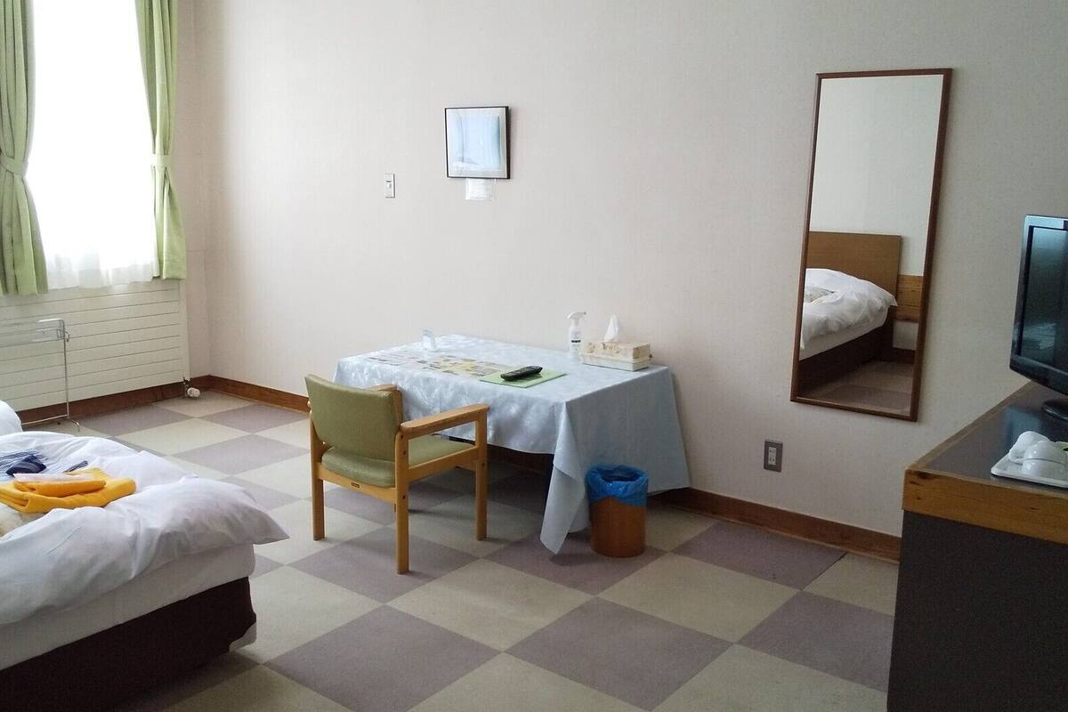 A hotel room with two beds, a desk with a chair, a mirror, and a television.
