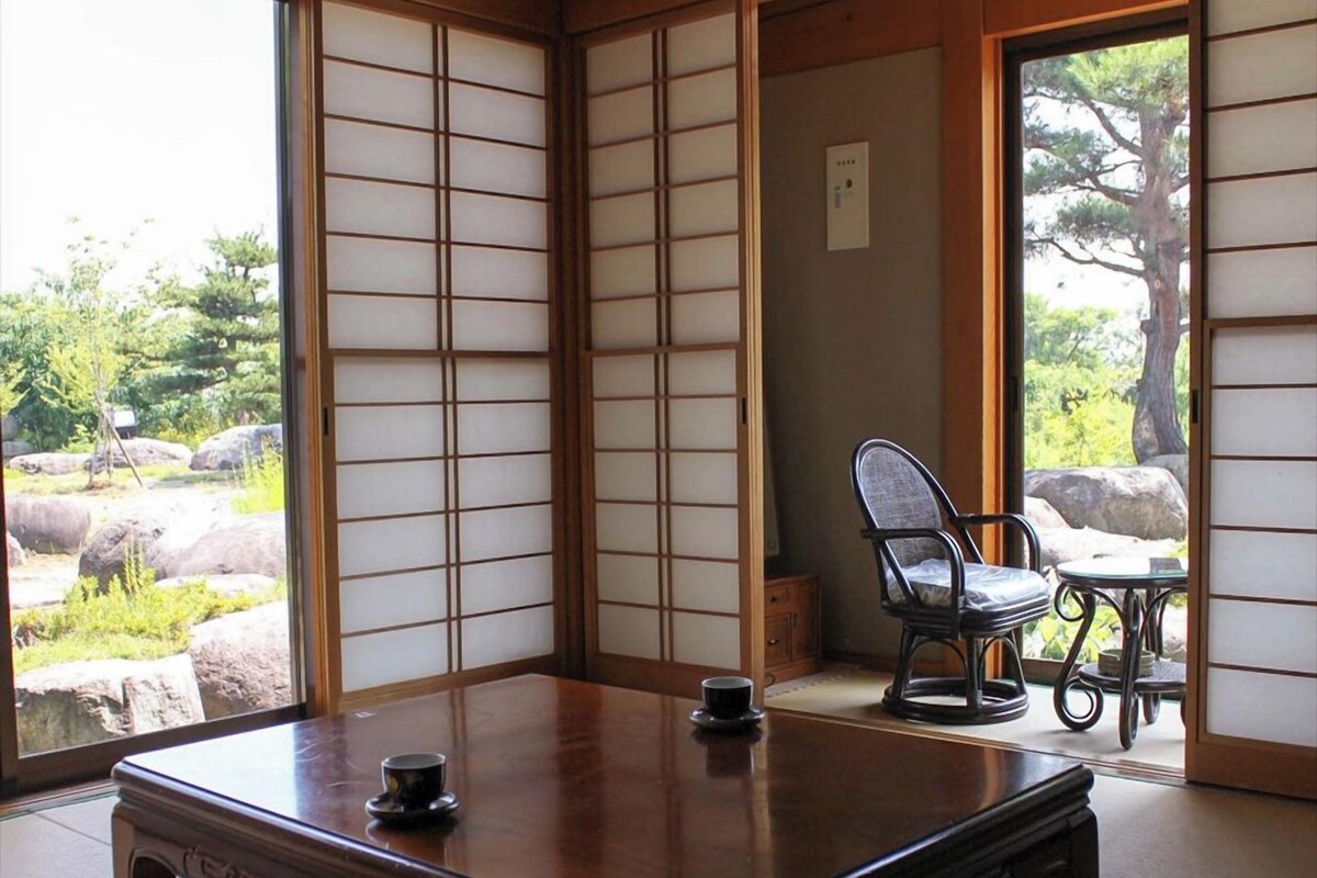 Una habitación japonesa tradicional con suelo de tatami, una mesa de madera baja y vistas a un jardín a través de biombos shoji.