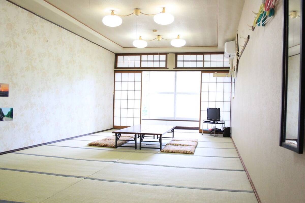 Una habitación con esteras tatami, una mesa baja, un sofá y un televisor sobre un mueble bajo.