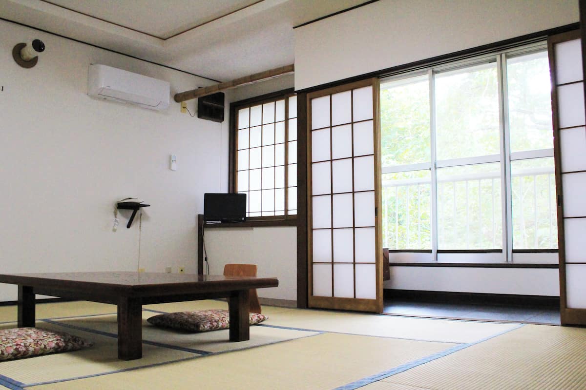 Una habitación con esteras de tatami, una mesa baja, un televisor en una estantería y una puerta corredera shoji.