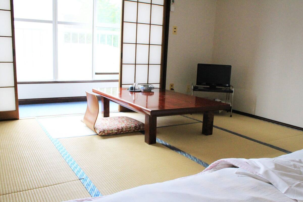 Una habitación con tatami, una mesa de madera baja, un cojín y un televisor.