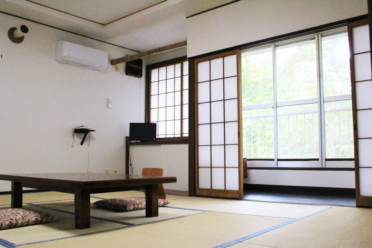 Una habitación con tatami, una mesa baja, una puerta corrediza y un televisor en la pared.