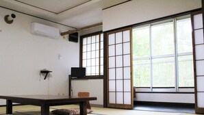 A tatami mat room with a low table, a TV on a shelf, and a sliding shoji door. - Shokanto Onsen Ryokan (Owani)