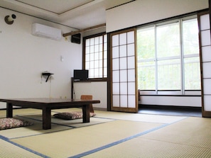 A tatami mat room with a low table, a TV on a shelf, and a sliding shoji door. - Shokanto Onsen Ryokan (Owani)