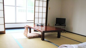 A traditional Japanese room with tatami flooring, a low wooden table, a cushion, and a television. - Shokanto Onsen Ryokan (Owani)