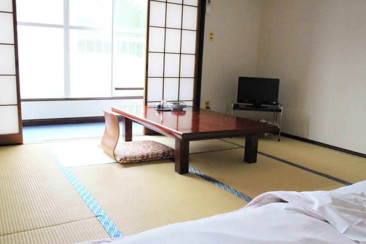 Una habitación japonesa tradicional con suelo de tatami, una mesa de madera baja, un cojín y un televisor.
