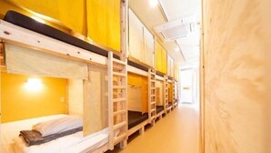 A row of bunk beds in a dormitory room with yellow walls and wooden flooring. - Million Pointz <amami Oshima> (Amami)