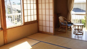 Um quarto japonês tradicional com tatames, um painel shoji, uma cadeira de madeira com almofada e uma pequena mesa redonda.