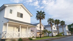 A row of white houses with a porch, palm trees, and a clear sky.