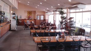 A restaurant with wooden tables and chairs, a counter with a refrigerator, and a large window with a view.